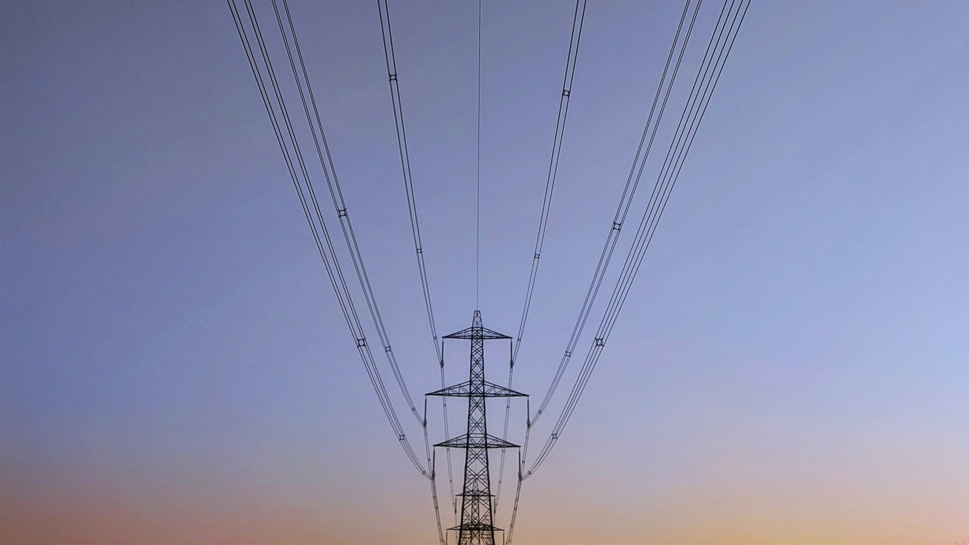 An electricity transmission tower and overhead lines. Photo by Hannah Wright on Unsplash.
